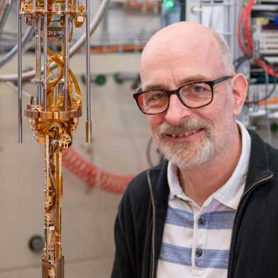 Klaus Ensslin steht lächelnd vor einem Quantencomputer