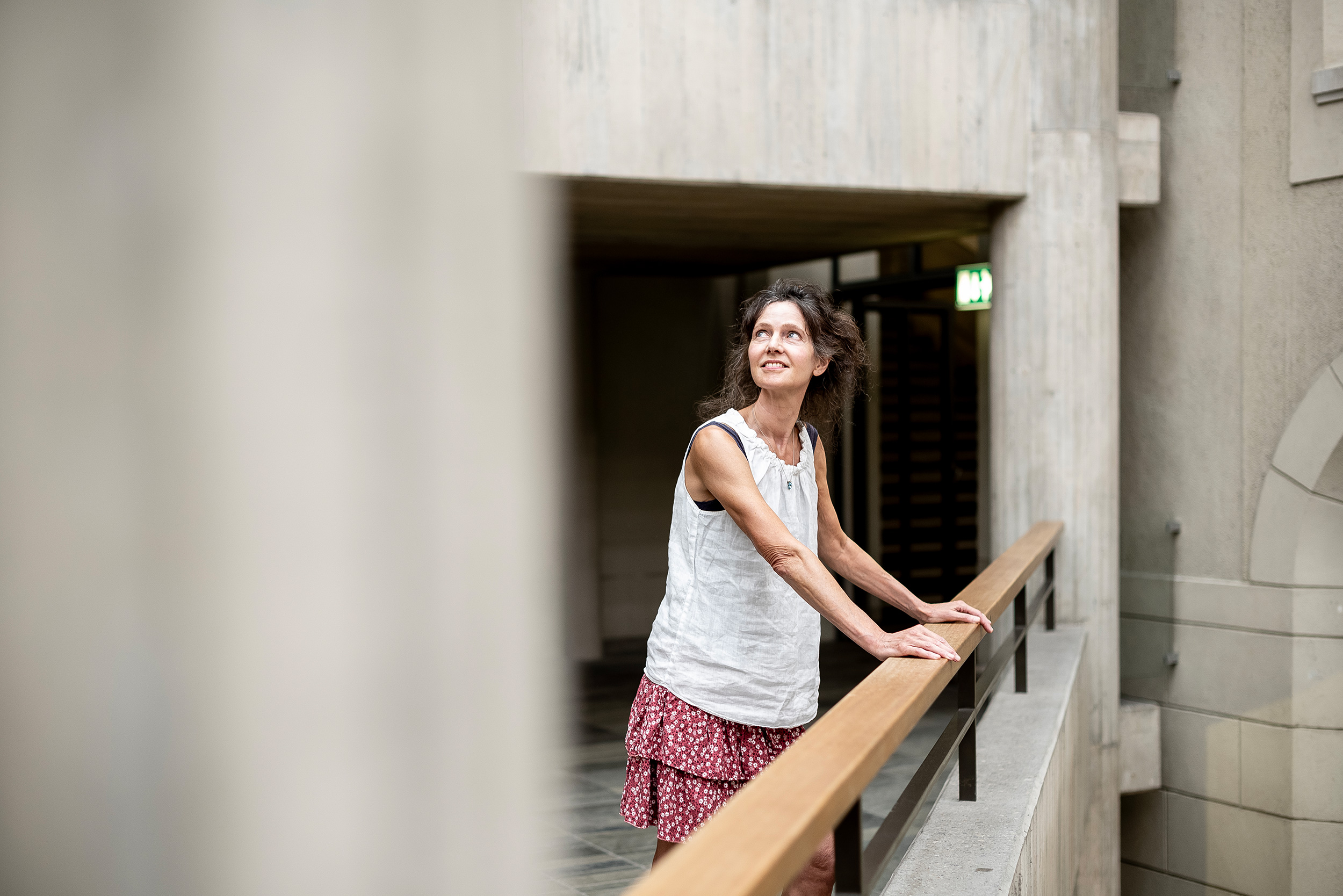 Sara van der Geer im ETH Zentum Gebäude, sie stützt sich am Geländer ab und schaut lächelnd zur Decke hoch.