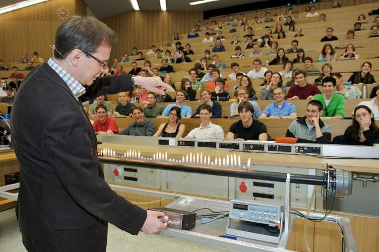 Vergrösserte Ansicht: Ein Professor führt im Hörsaal Experiment durch. Studierende schauen ihm von den Bänken aus zu.