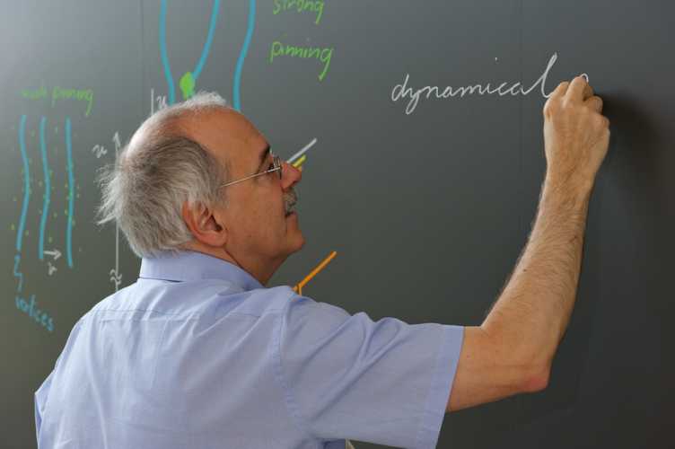 Physik ist Grundlagenwissenschaft. Ein Professor schreibt Formeln an die Wandtafel. 