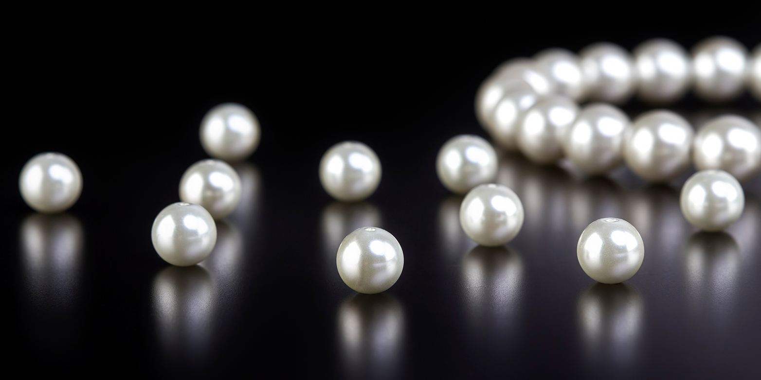 A white pearl necklace and single pearls on a black table