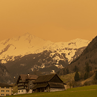Residential houses with mountain landscape in the background, with everything bathed in orange light.