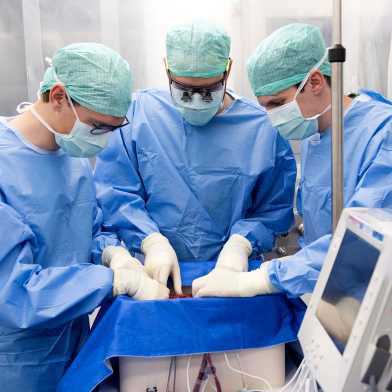 Three surgeons are bent over the perfusion machine