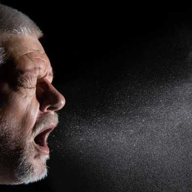 Man coughing, aerosol particles floating in the air in front of him