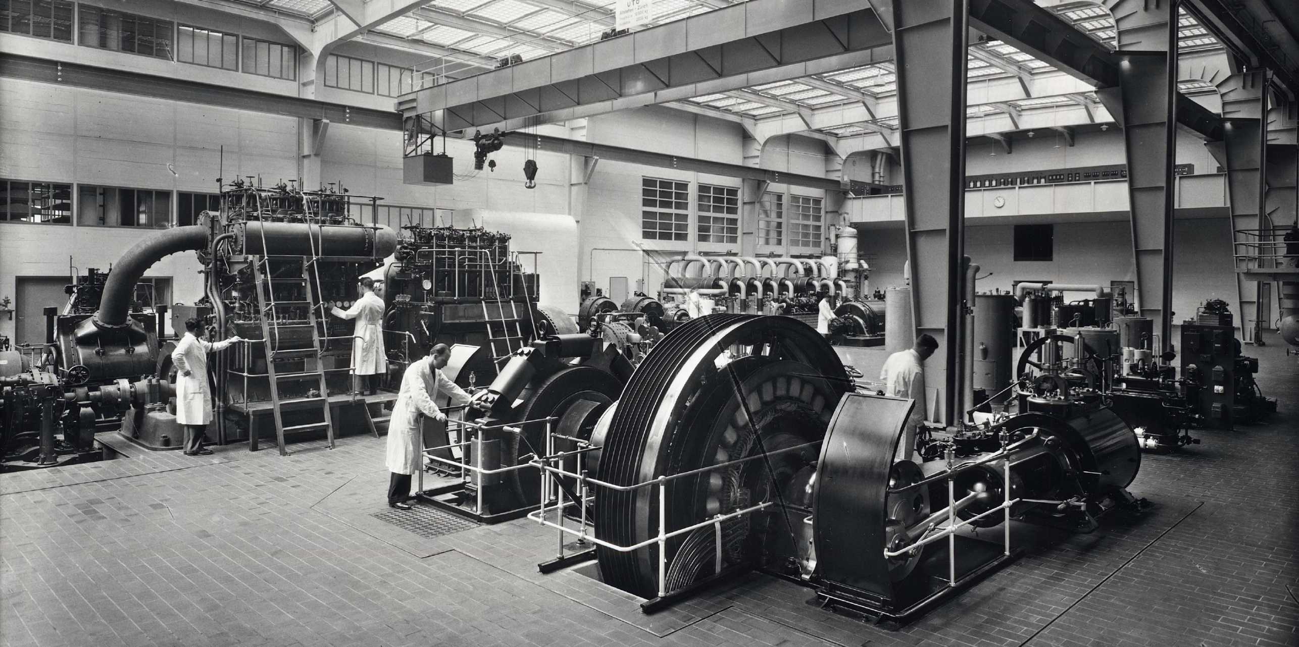 Old black and white picture of a factory building, people working on the machines.