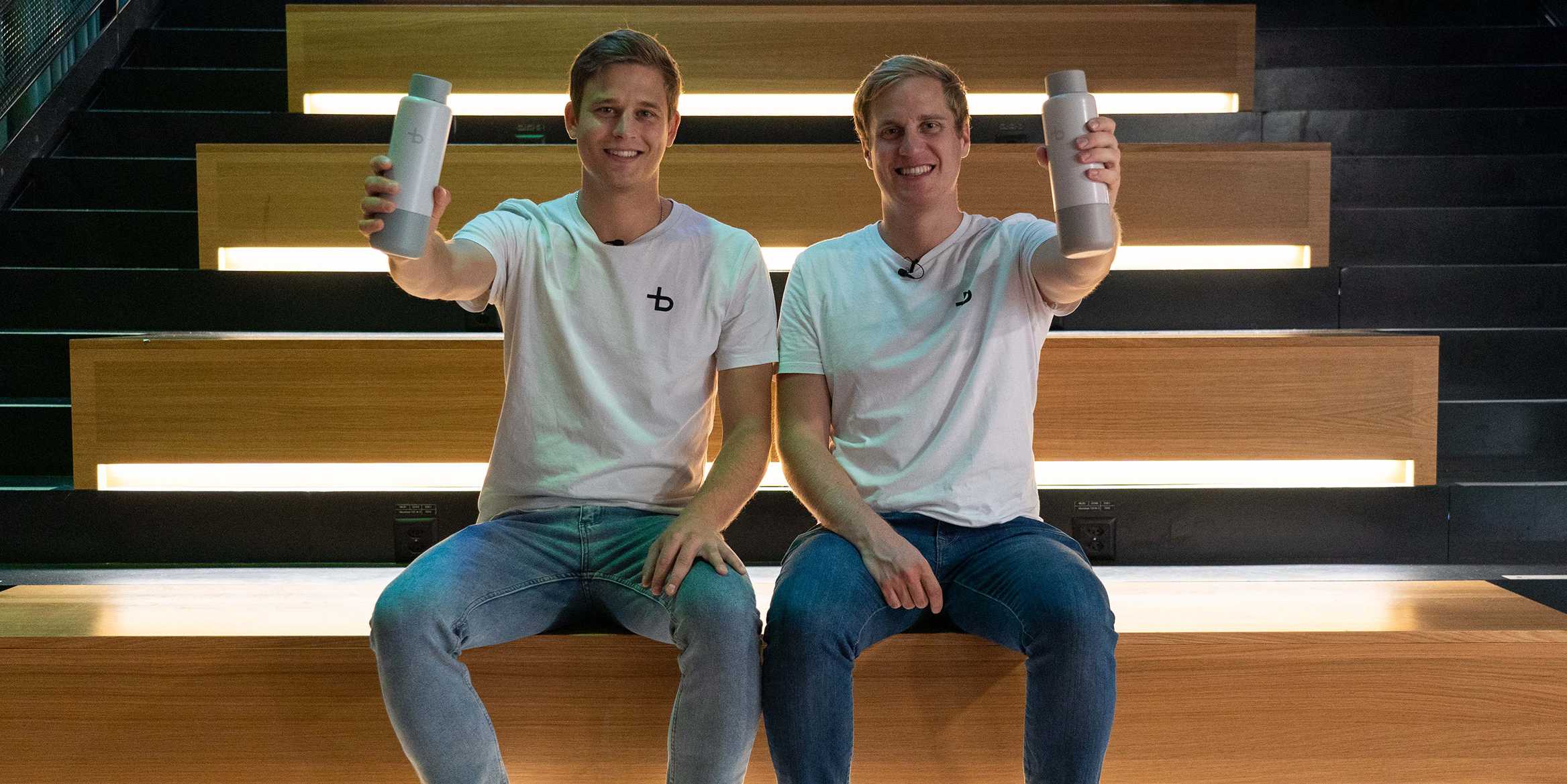 Christian Käser and Linus Lingg are sitting on a staircase holding up their Bottleplus bottle.