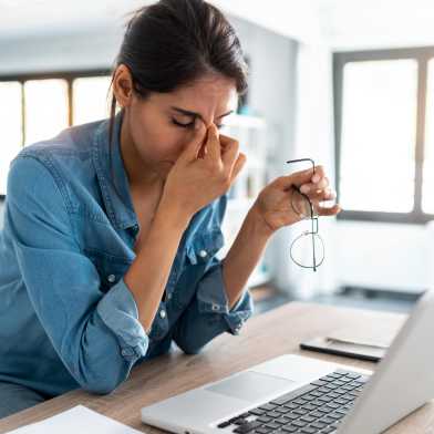 Woman sits in front of the computer and rubs her nose.