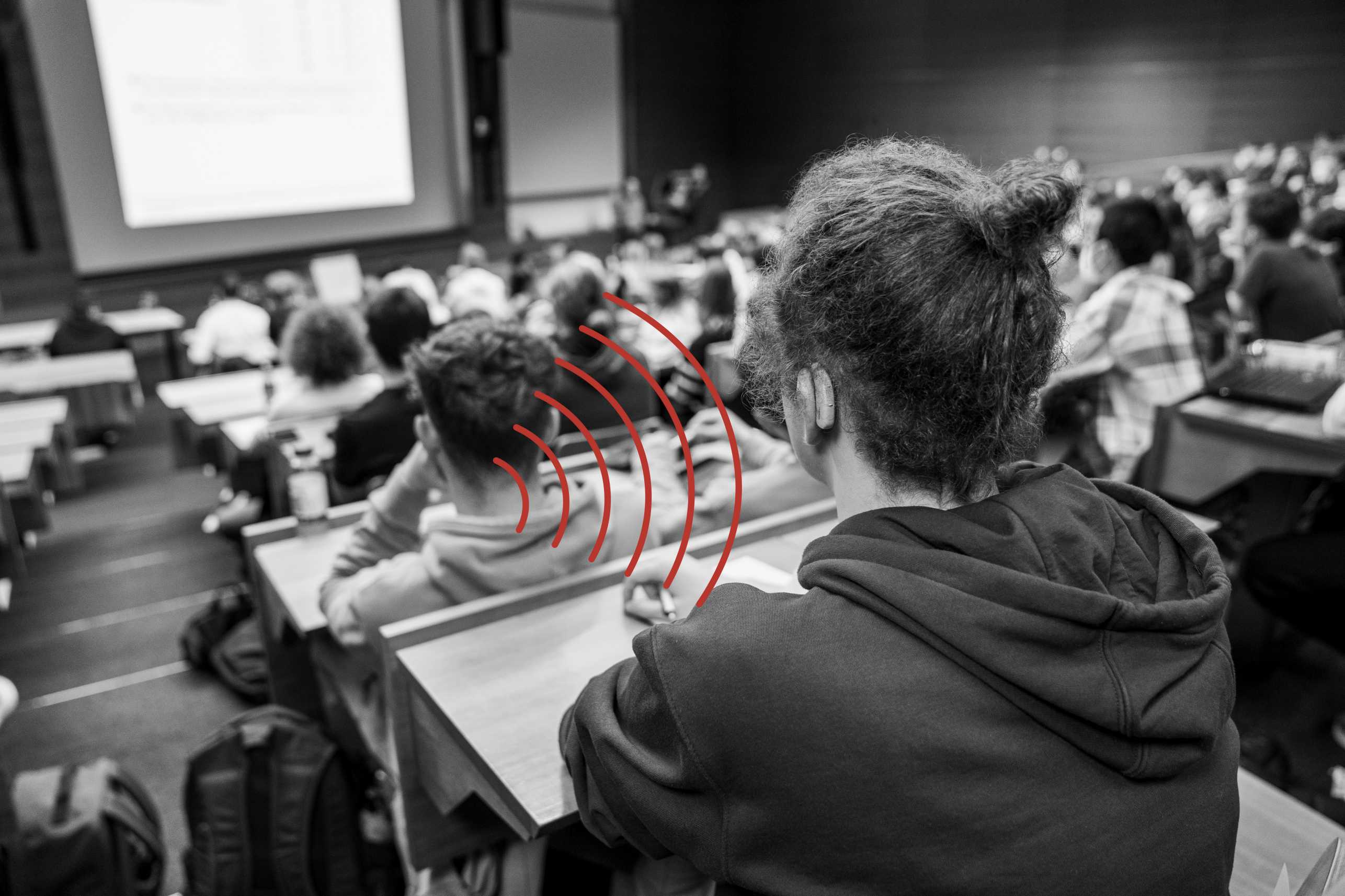 Vergrösserte Ansicht: In einem Hörsaal voller Studierenden sitzt ein Student mit einem Hörgerät, welches die akustischen Signale über eine Induktionsschlaufe aufnimmt. 