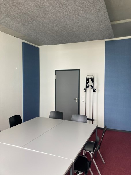 Vergrösserte Ansicht: Sitzungszimmer, ausgestattet mit einem grauen Deckensegel und blauen Wandabsorbern in drei Ecken des Raumes.