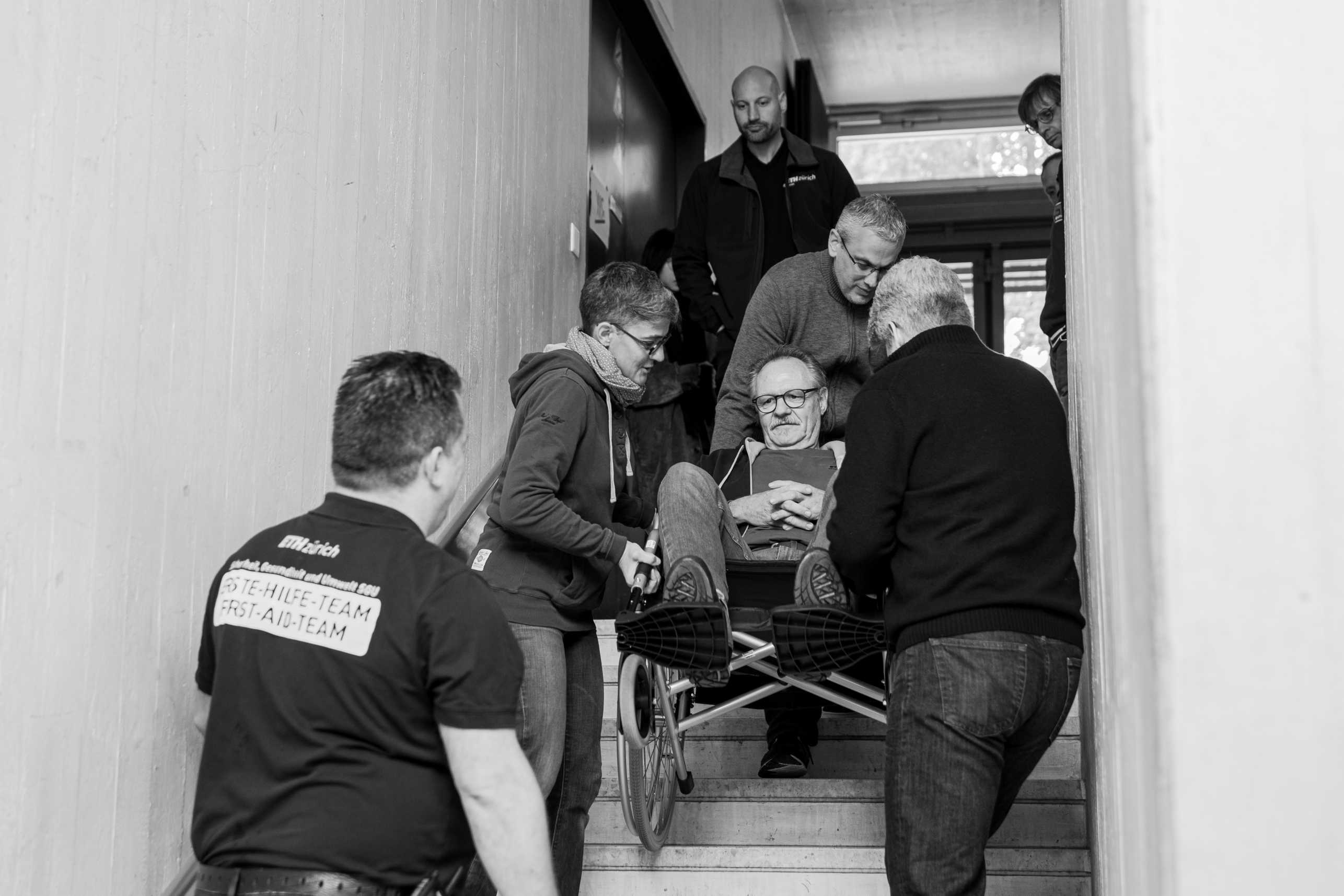 A group of people evacuate a man in a wheelchair via the stairwell.