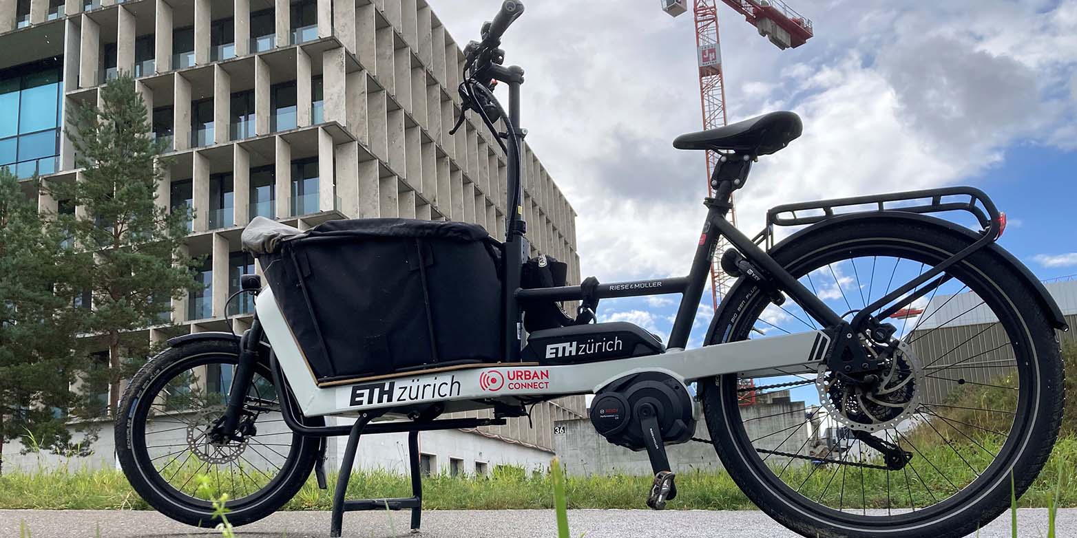 The e-cargo bike in front of a meadow, with building and crane