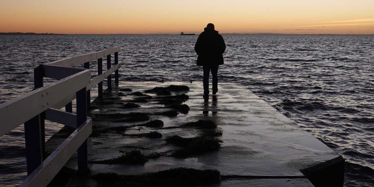 Man standing on a dock looking across the water into the sunset.