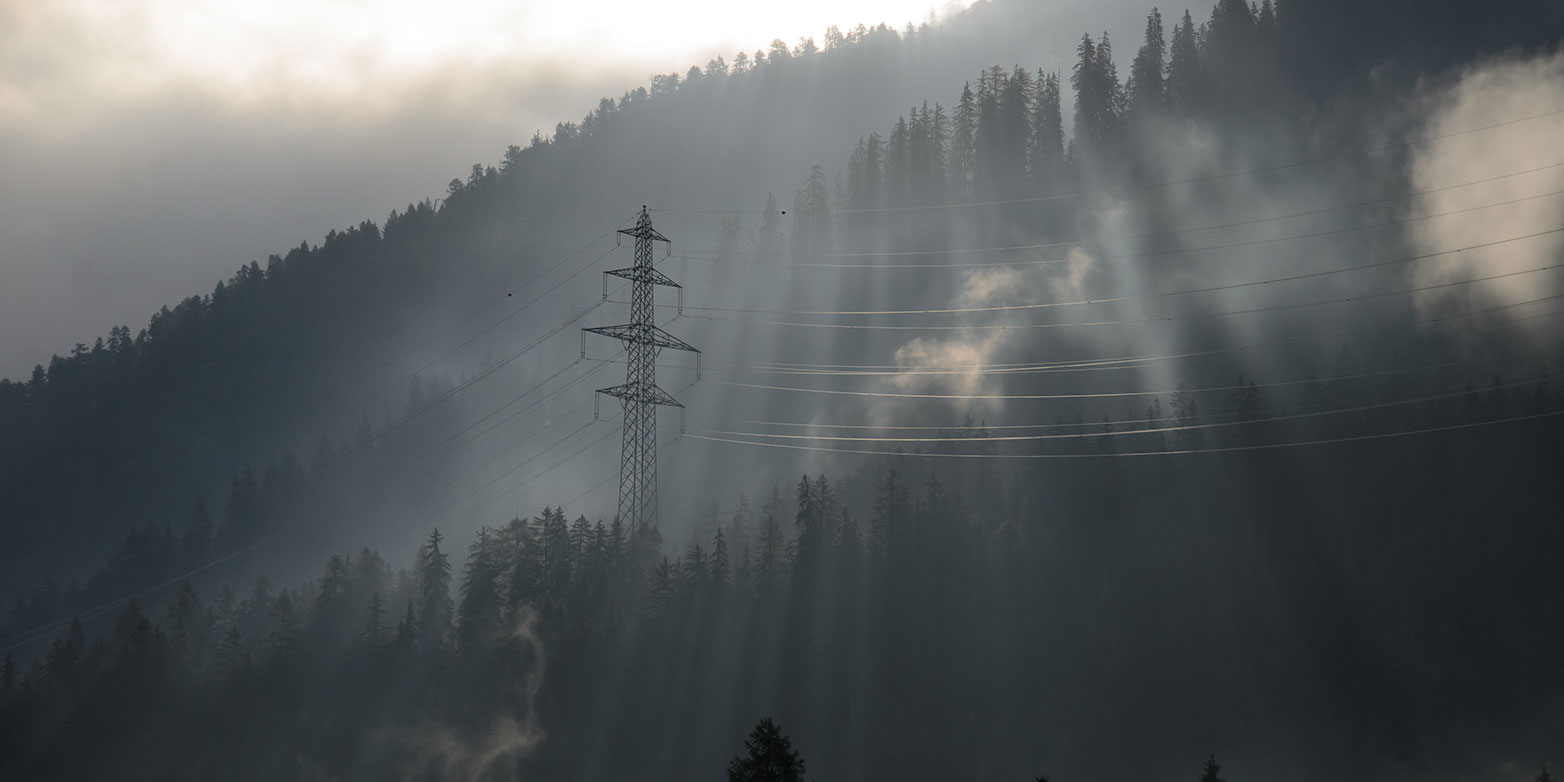 Power grid with pylon in the Swiss Alps surrounded by light and fog
